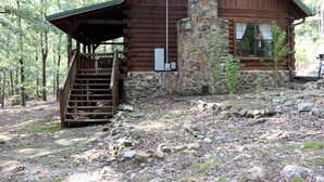 Une cabane en rondins avec une cheminée en pierre, un escalier en bois et une fenêtre donnant sur la forêt.