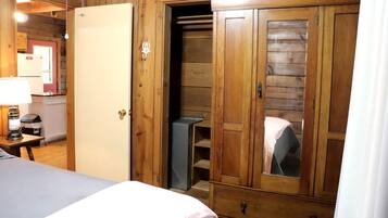 Una habitación de madera con una cama, un armario, un escritorio con una lámpara y una mesita.