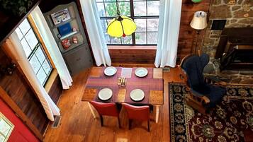 A dining area with a wooden table set for four, a hanging lamp, and a view through a window.