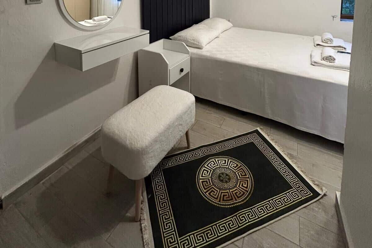 Un dormitorio con cama, mesita de noche, espejo, equipo de aire acondicionado y una alfombra decorativa.
