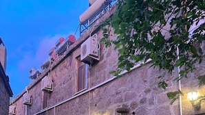 A stone building with multiple windows, a door, and a small garden area. - Assos Elit Pansiyon (Ayvacik)