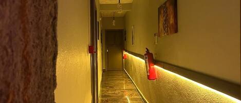 A hallway with a marble floor, ceiling fans, and wall-mounted fire extinguishers.