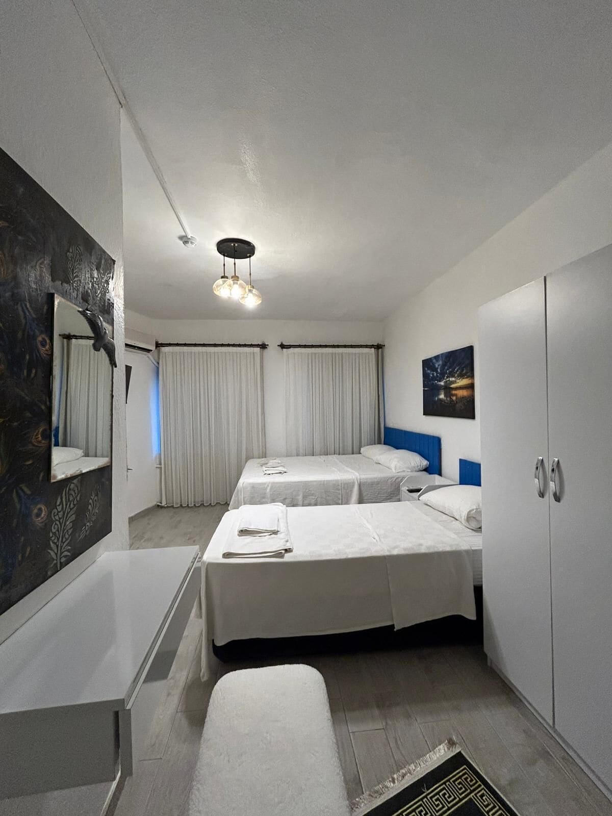 A hotel room with two beds, a desk, a wardrobe, a mirror, and a ceiling light fixture.