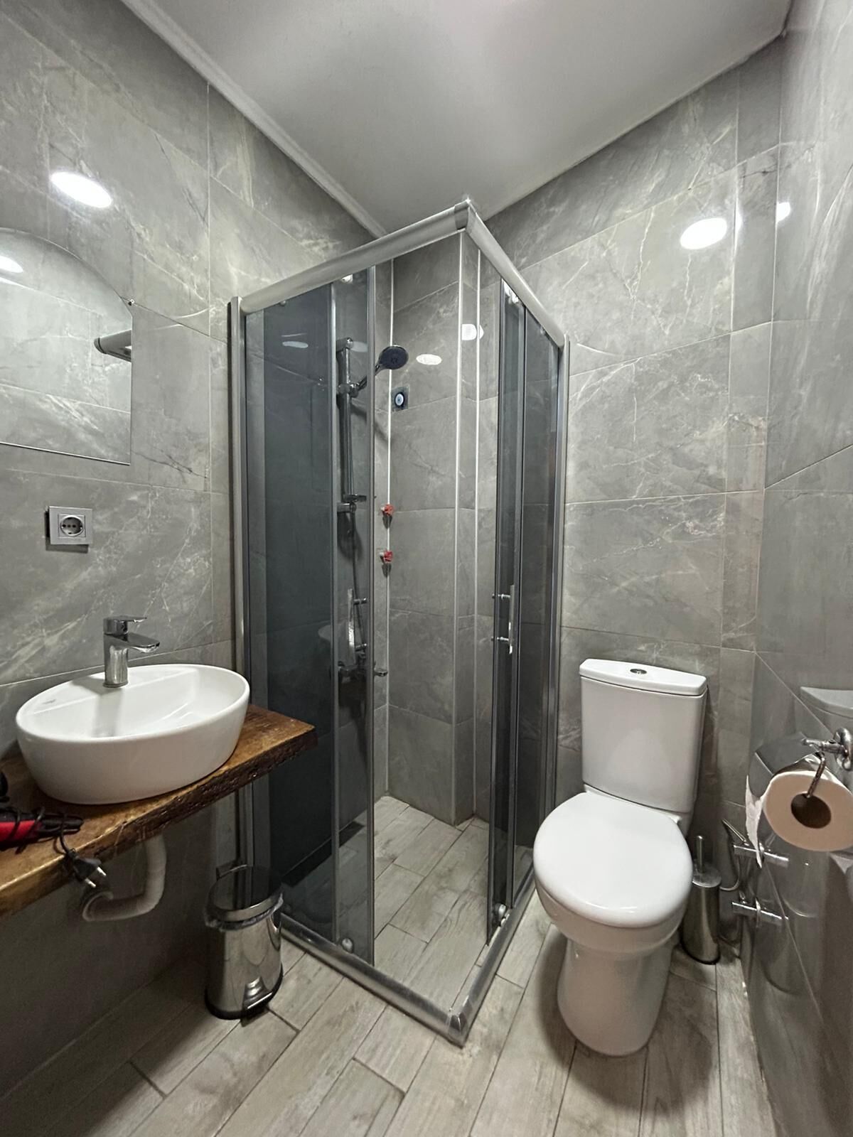A modern bathroom with a glass-enclosed shower, a white sink, and a toilet.