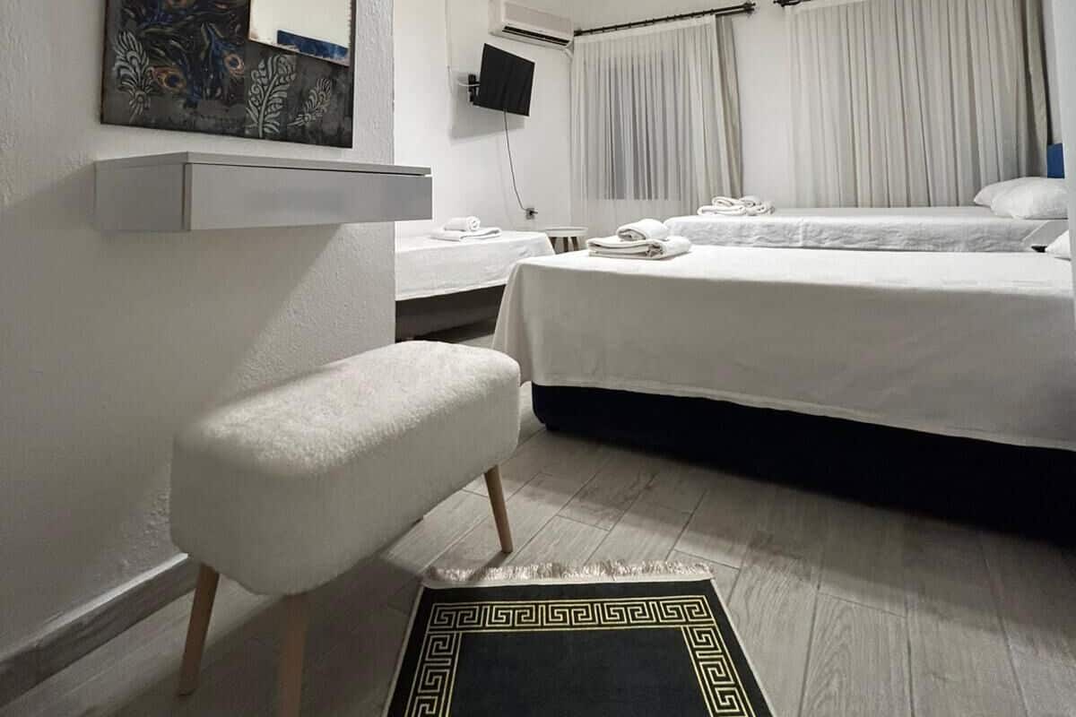 Habitación de hotel con cama, un banco, televisor y un espejo decorativo.