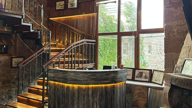 A wooden interior with a central wooden staircase, a chandelier, and a stone fireplace. - Assos Elit Pansiyon (Ayvacik)