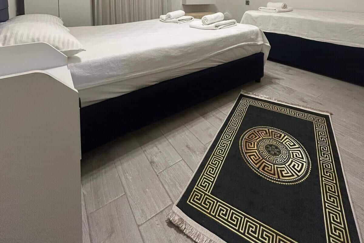 Un dormitorio con cama, mesitas de noche, armario, unidad de aire acondicionado, un cuadro y una alfombra estampada.