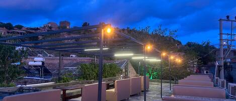 A rooftop terrace with outdoor seating, a pergola with string lights, and a view of the surrounding landscape.