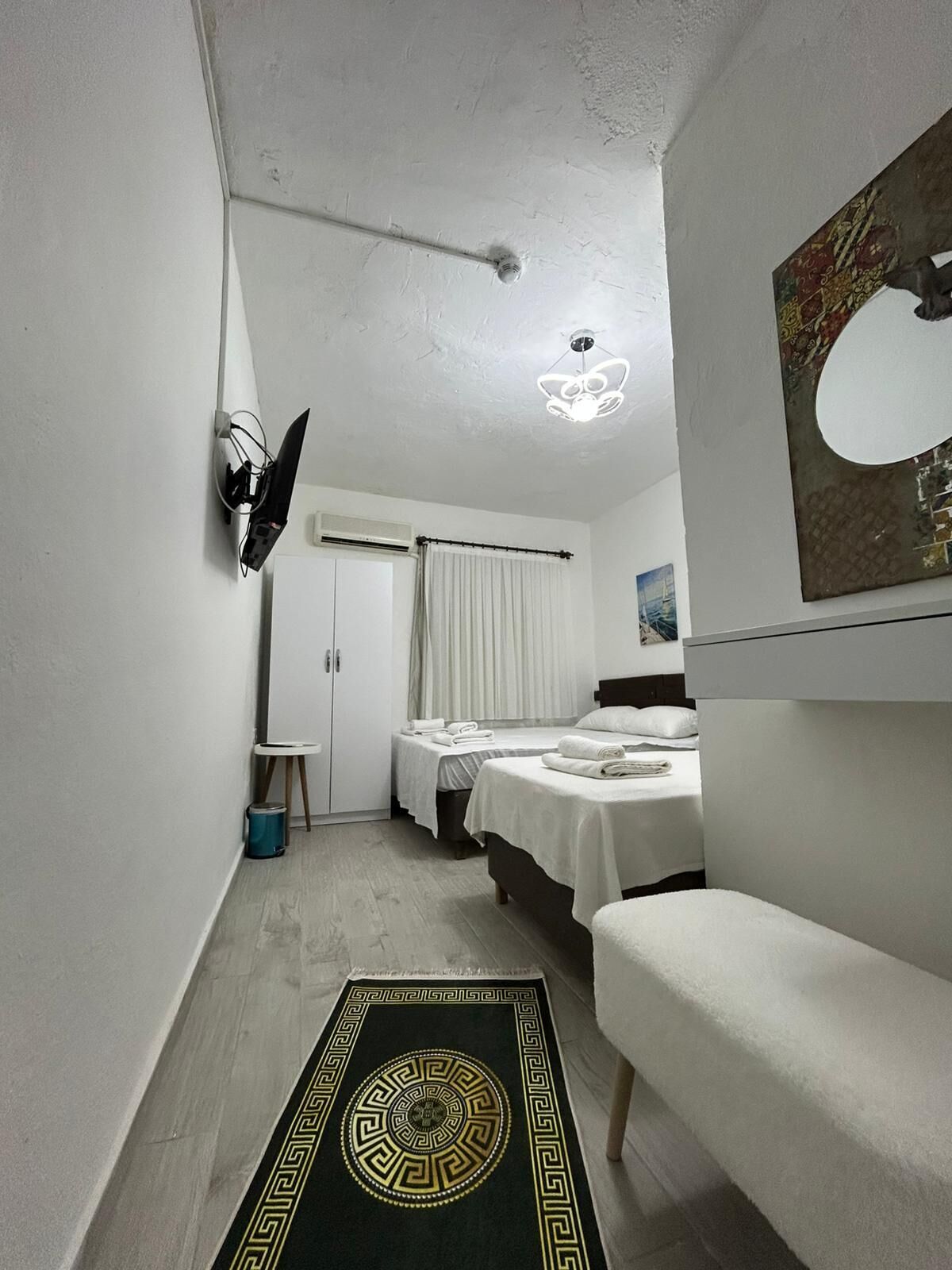 A hotel room with a bed, a small table, a mirror, and a ceiling light.