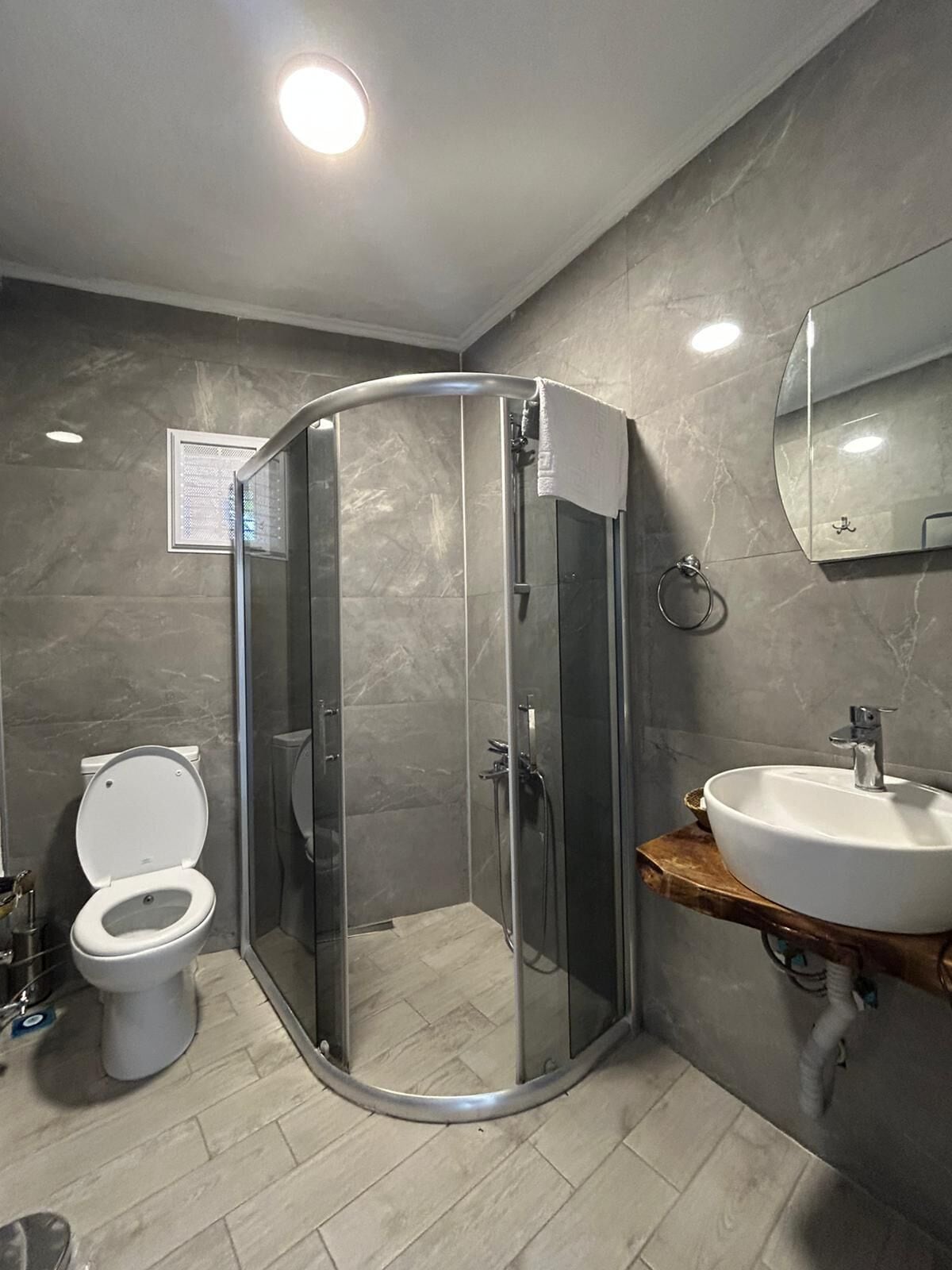 A modern bathroom with a glass shower enclosure, a toilet, and a sink with a wooden countertop.