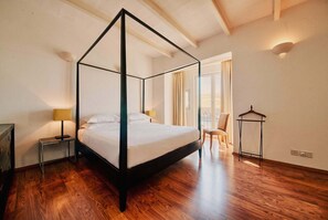 A four-poster bed in a room with wooden flooring, a nightstand, a chair, and a hanging rack. - Valletta Postcard Penthouse (Il-Belt Valletta)