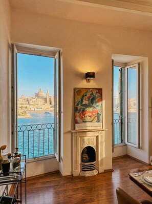 A room with a fireplace, a painting, and a view of a cityscape through large windows. - Valletta Postcard Penthouse (Il-Belt Valletta)