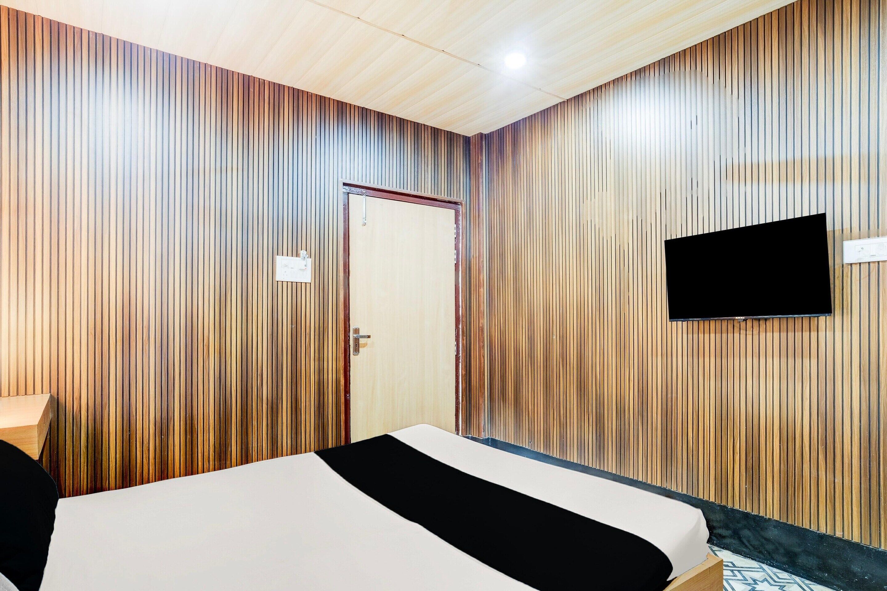 A hotel room with a bed, a television mounted on the wall, and a door.