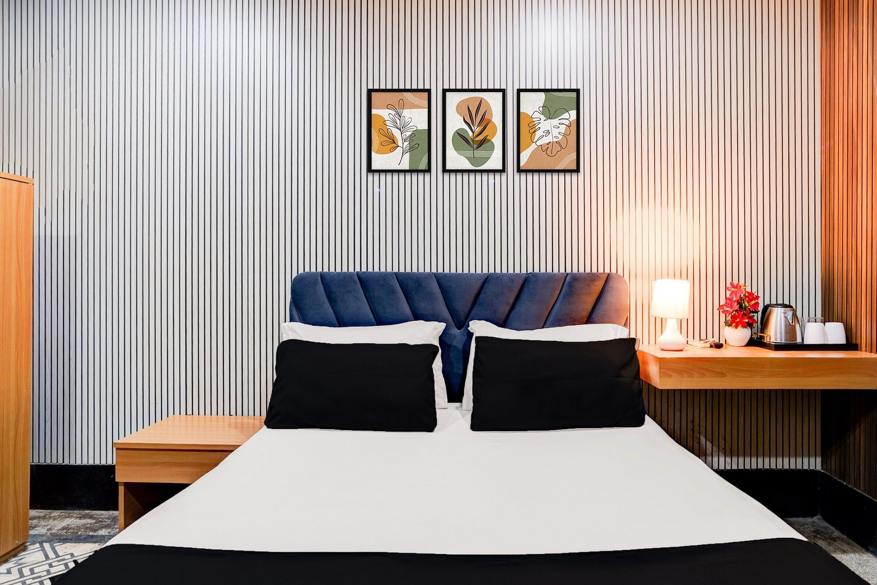 Una habitación de hotel con cama, mesita de noche, lámpara y cuadros en la pared.