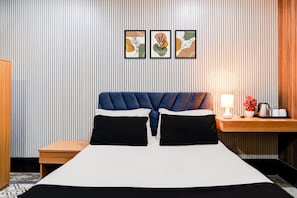 Una habitación de hotel con cama, mesita de noche, lámpara y cuadros en la pared.