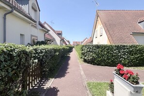 Eine schmale Wohnstraße mit Häusern, einem gepflasterten Weg und einer Hecke an einer Seite.