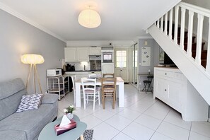 Ein modernes Wohnzimmer mit einem grauen Sofa, einem Esstisch mit Stühlen, einer Küchenzeile mit weißen Schränken und einer Treppe mit weißen Geländern.