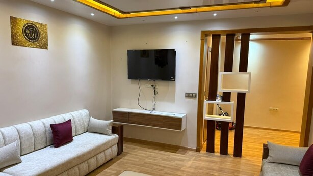 Una sala moderna con sofá, reposapiés, televisor y estante en la pared.