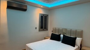 Un dormitorio con cama, mesitas de noche, una ventana y una lámpara en el techo.