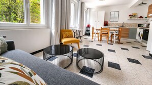 Ein modernes Wohnzimmer mit einer Couch, zwei runden Tischen, einem gelben Sessel und einem Essbereich mit einem Holztisch und Stühlen.