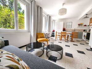 Ein modernes Wohnzimmer mit einer Couch, zwei runden Tischen, einem gelben Sessel und einem Essbereich mit einem Holztisch und Stühlen.