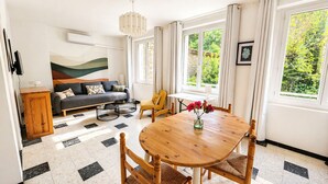 Ein Wohnzimmer mit Sofa, einem Esstisch mit Stühlen, einem Fernseher und einem Gemälde an der Wand.