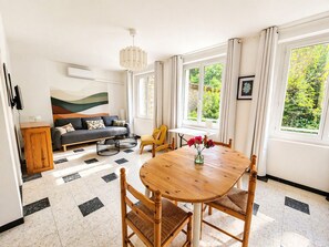 Ein Wohnzimmer mit Sofa, einem Esstisch mit Stühlen, einem Fernseher und einem Gemälde an der Wand.