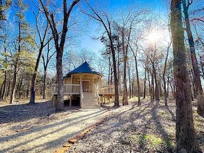 Une cabane en bois dotée d’un porche et d’un escalier, entourée d’arbres au cœur d’une forêt.