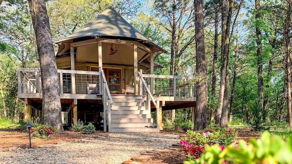 A wooden cabin with a conical roof, a balcony, and a staircase leading to the entrance.