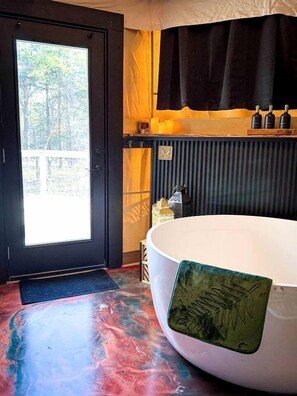 Ein Zimmer mit einer großen Badewanne, einer Tür, die nach draußen führt, einem Heizkörper und einem kleinen Regal mit Flaschen.