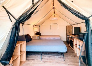 Ein Zeltraum mit Bett, Fernseher und Holzböden.