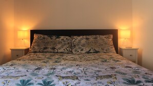 Ein Bett mit floralem Überwurf, zwei Nachttische mit Lampen und ein dunkles Kopfteil.