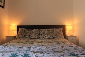 A bed with a floral-patterned bedspread, two bedside lamps, and a dark headboard. - Modern Central Apartment (Brighton and Hove)