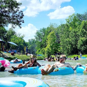People floating on water in a natural setting with trees and a clear sky.