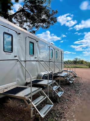 A row of mobile homes with external shower facilities, metal stairs, and a dirt ground.
