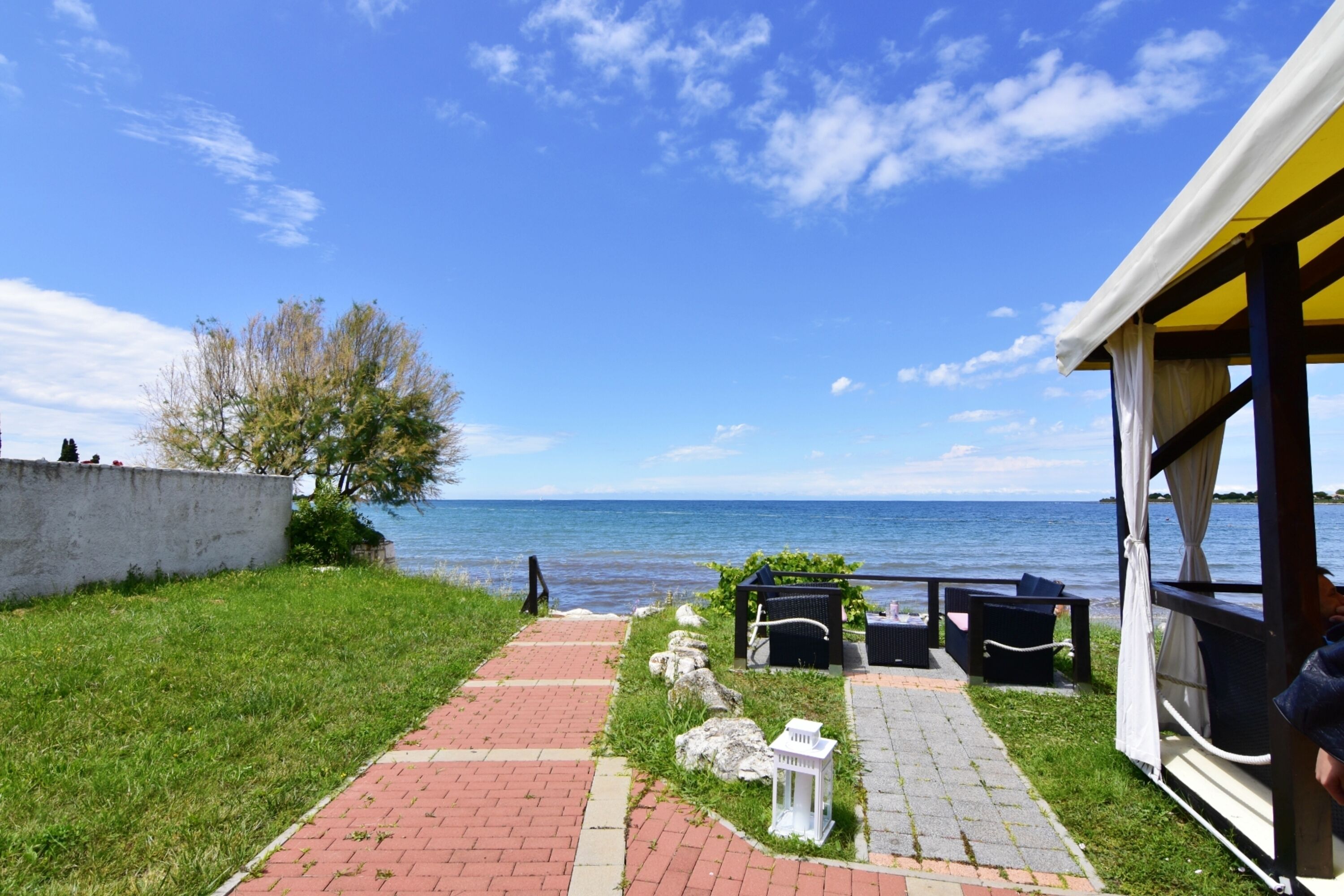 A pathway leading to a seaside view with a gazebo, seating area, and a view of the sea.