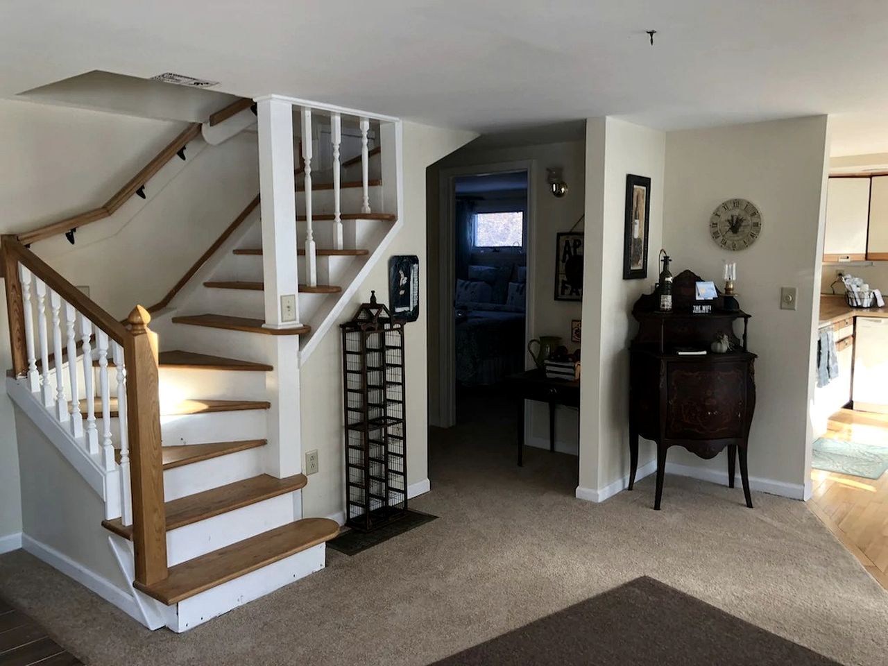 A staircase with wooden steps and white railings, a dark wooden side table with a clock, and a door leading to another room.