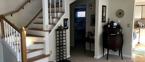 A staircase with wooden steps and white railings, a dark wooden side table with a clock, and a door leading to another room.