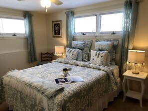 Ein Schlafzimmer mit einem Bett, zwei Nachttischen mit Lampen, einem Fenster mit Vorhängen und einem gerahmten Bild an der Wand.
