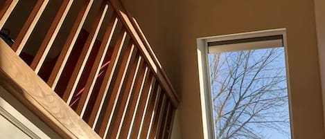 Een kamer met houten balkonbalustrade, een plafondventilator en een raam met uitzicht op bomen.