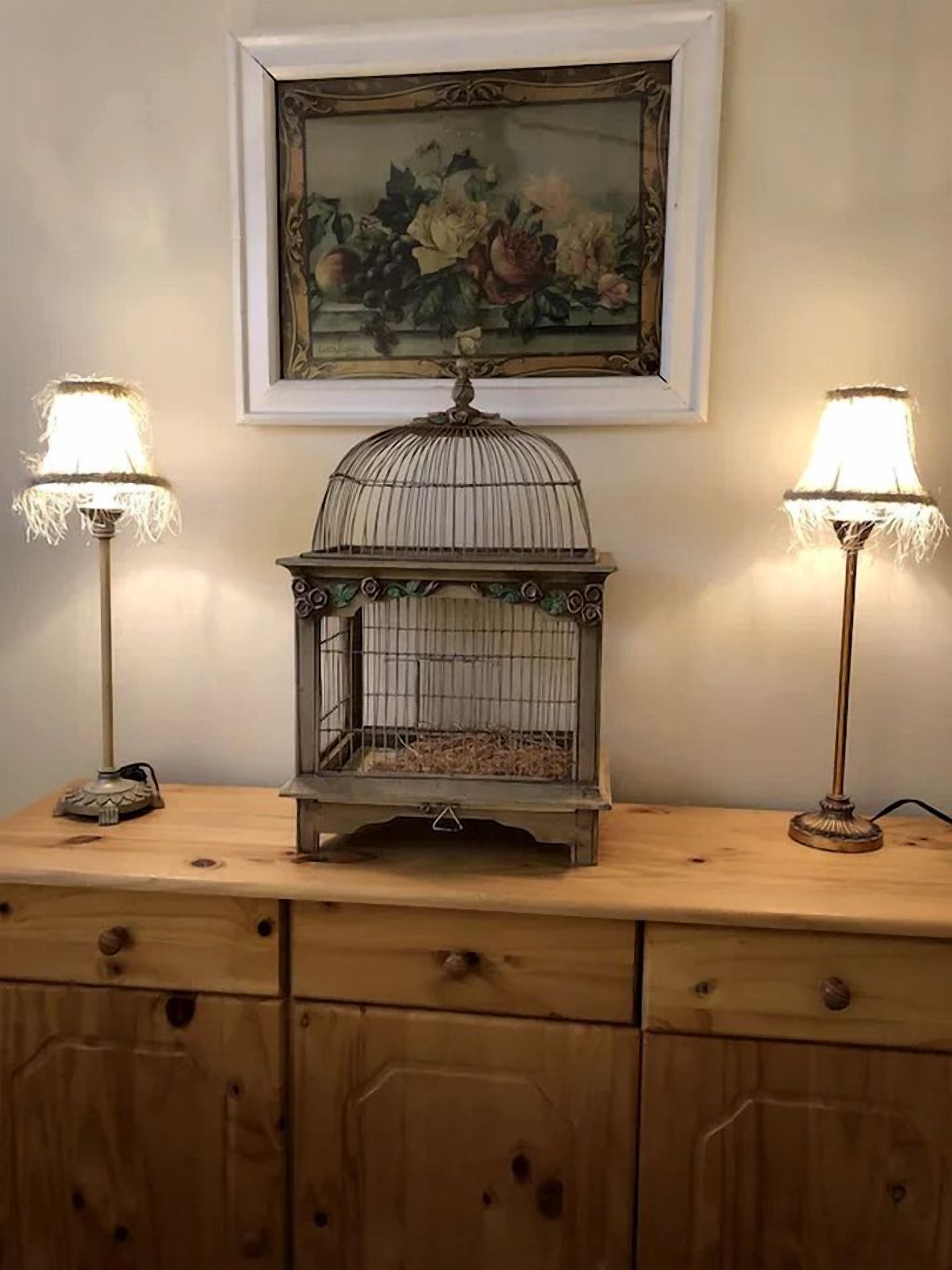 A wooden dresser with two lamps, a birdcage, and a framed painting on the wall.