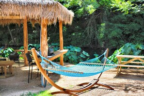 Eine Hängematte, Holzstühle, ein Tisch und eine strohgedeckte Struktur in einem Garten.