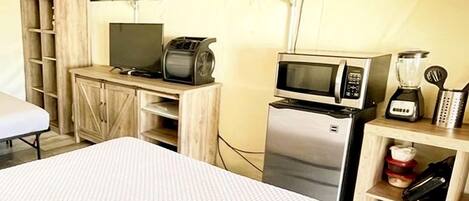 A tented accommodation with a bed, kitchenette, and a small table.