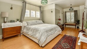 Une chambre à coucher comprenant un lit, une commode, une table de chevet, une lampe, des rideaux et un luminaire suspendu.