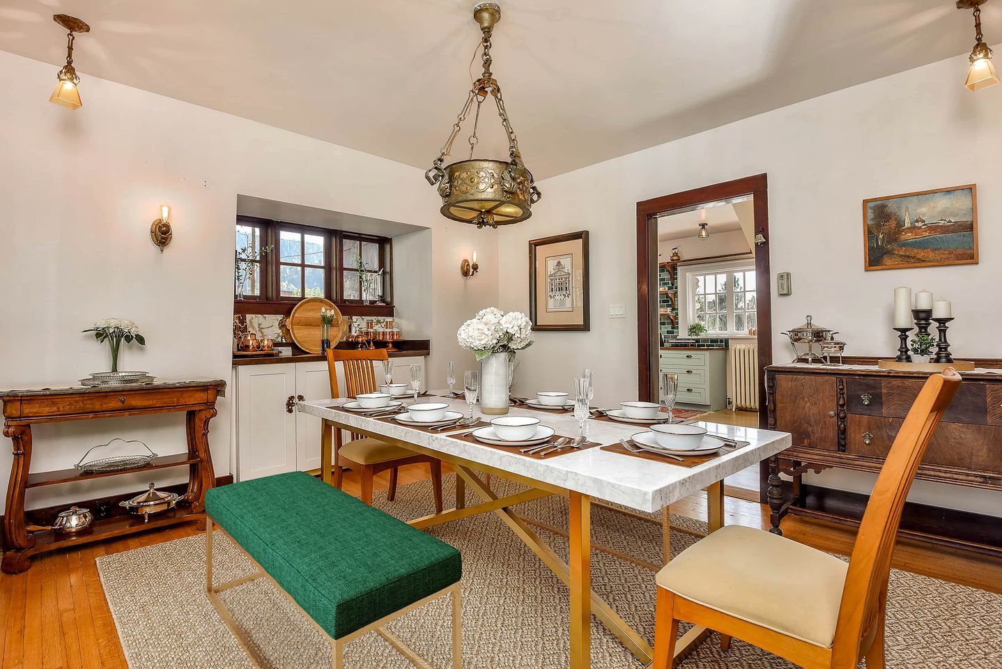 Una sala da pranzo con un tavolo in marmo apparecchiato per quattro persone, una panca verde, sedie in legno e un lampadario.