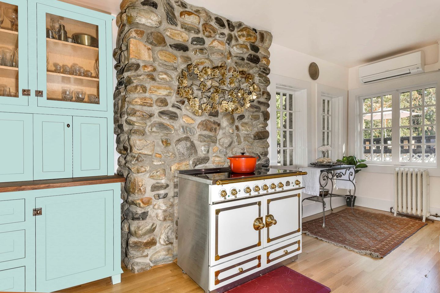 A kitchen with a stone wall, a stove, cabinets, and a window with a view.