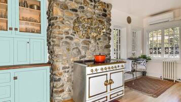 A kitchen with a stone wall, a stove, cabinets, and a window with a view.