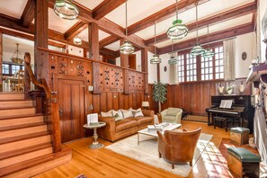A spacious living room with a grand staircase, wooden paneling, a piano, and a cozy seating area. - Elegance by the River: Classic Rental with Scenic Views in Metaline Falls, WA (Metaline Falls)