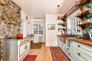 A kitchen with a stone wall, a stove, a sink, and wooden cabinets.