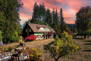 A rustic house with a stone foundation, green and brown exterior, and a porch with a wooden bench. - Elegance by the River: Classic Rental with Scenic Views in Metaline Falls, WA (Metaline Falls)